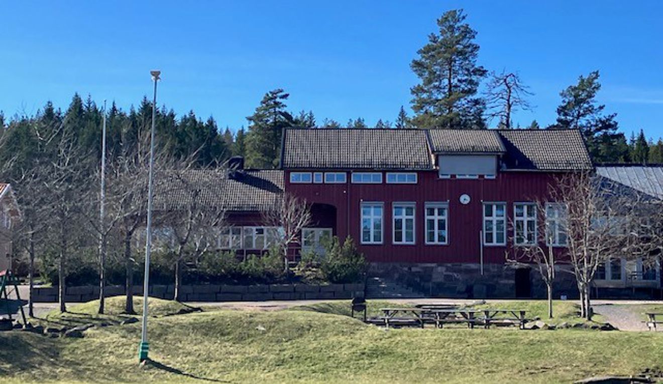En rød bygning med plen og trær foran