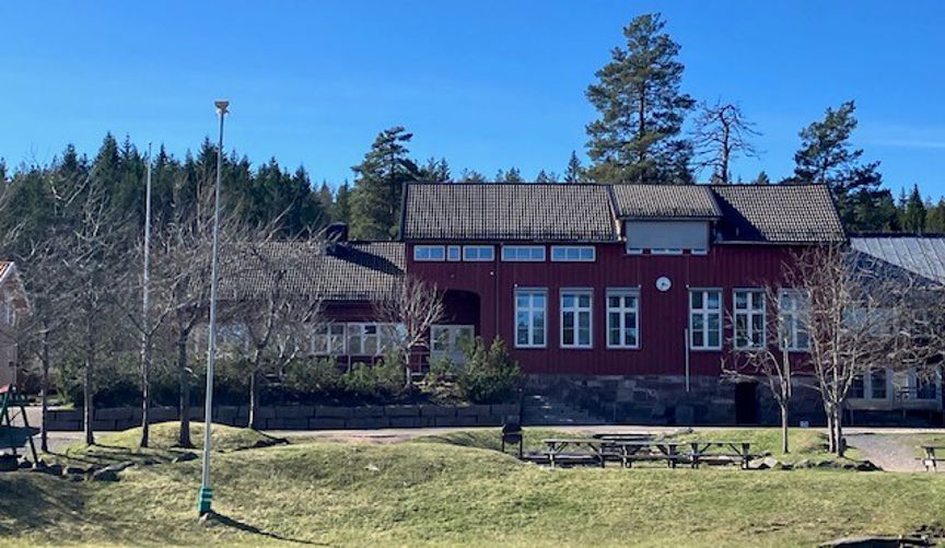 En rød bygning med plen og trær foran