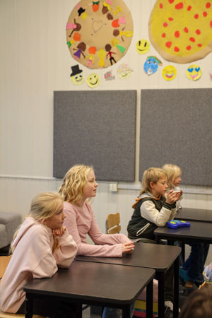 en gruppe barn som sitter ved pulter i et klasserom