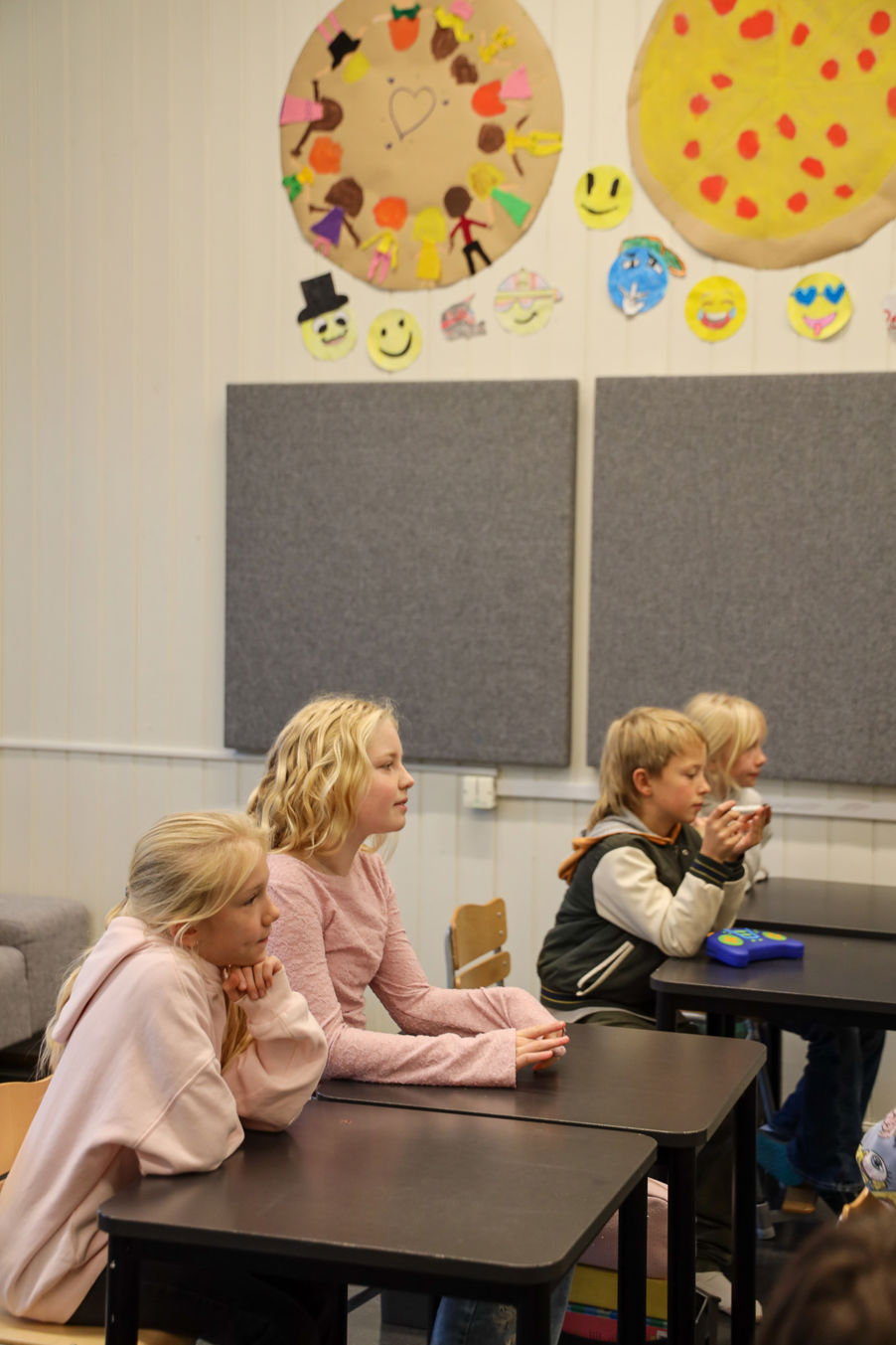 en gruppe barn som sitter ved pulter i et klasserom en gruppe barn som sitter ved pulter i et klasserom